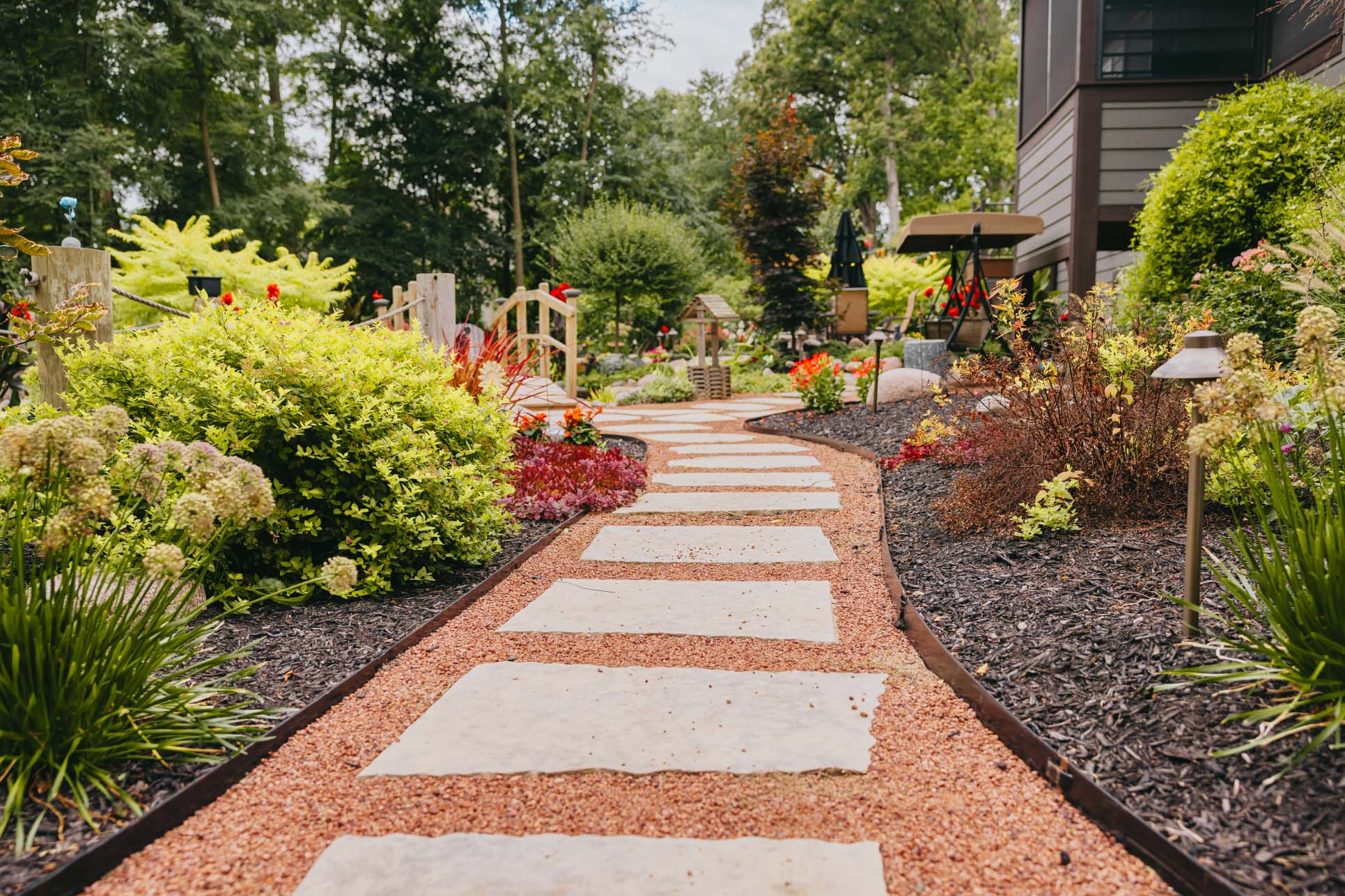 Curved garden pathway made of stone pavers surrounded by vibrant plants and mulch