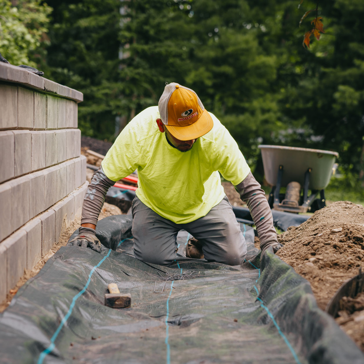 Professional landscaper laying down weed barrier fabric beside a retaining wall during landscape prep in the Chicago suburbs.