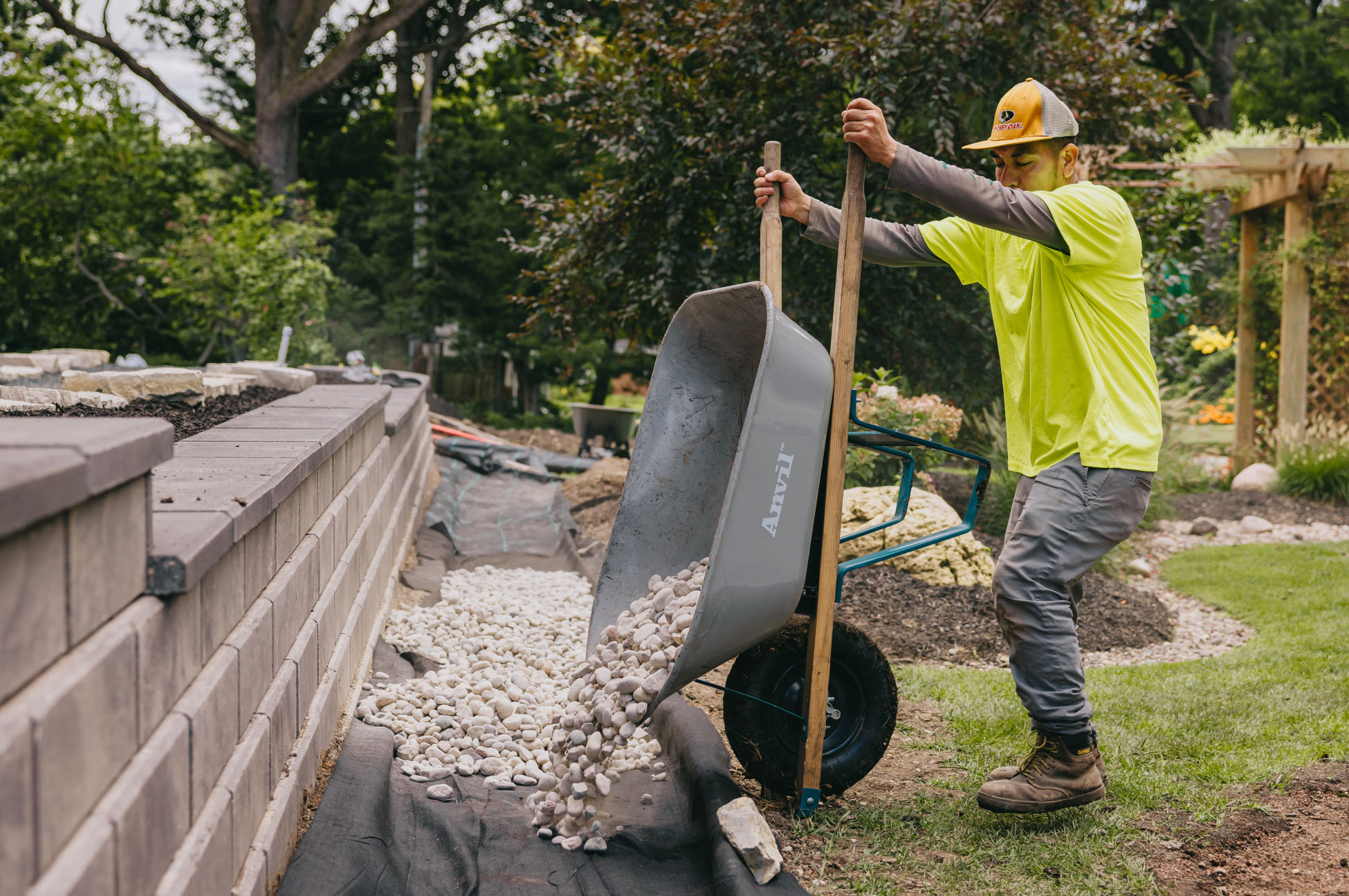 Landscaper pouring white decorative stones from a wheelbarrow beside a new retaining wall in suburban Chicago.