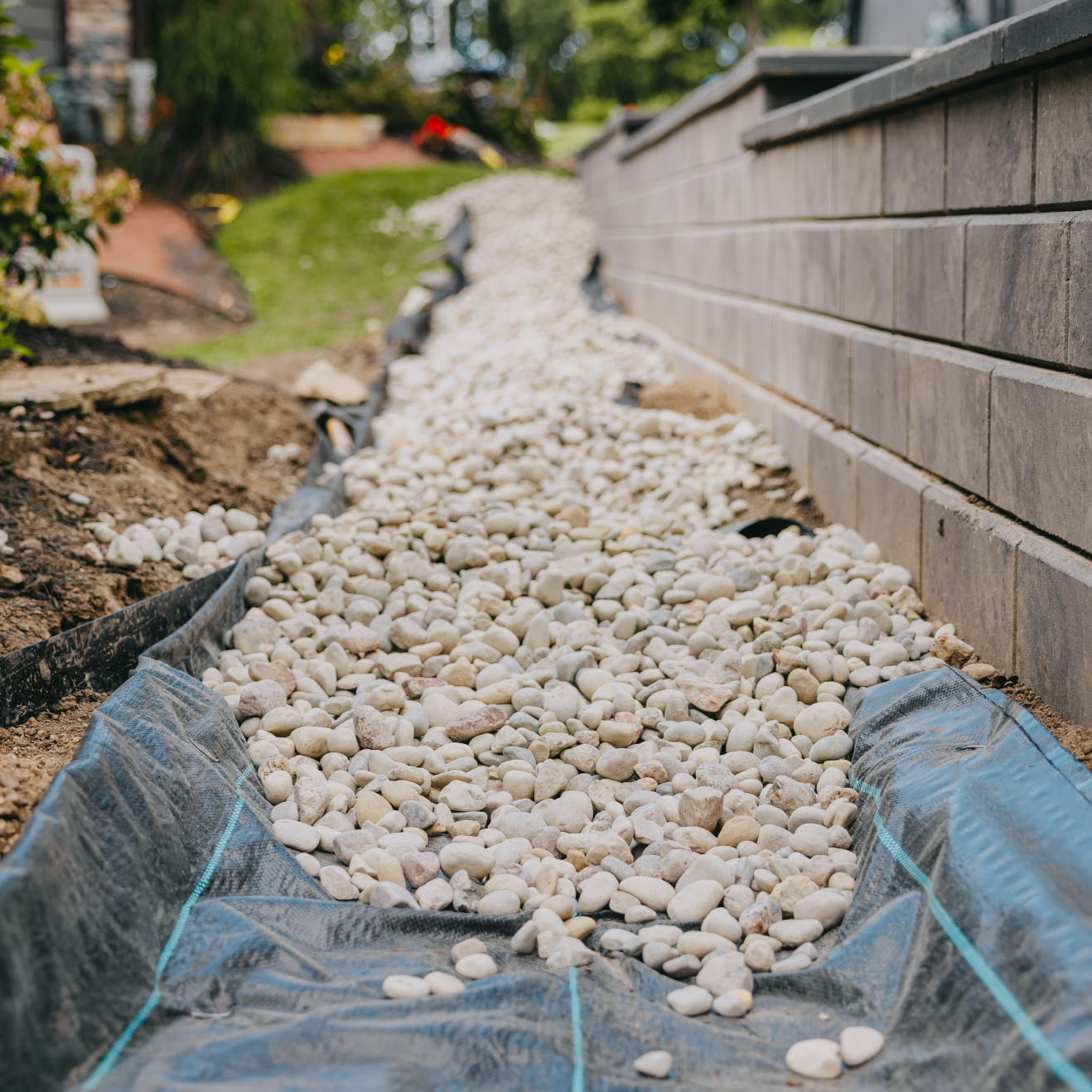 White decorative stones placed in a trench beside a retaining wall for drainage installation in the Chicago suburbs.