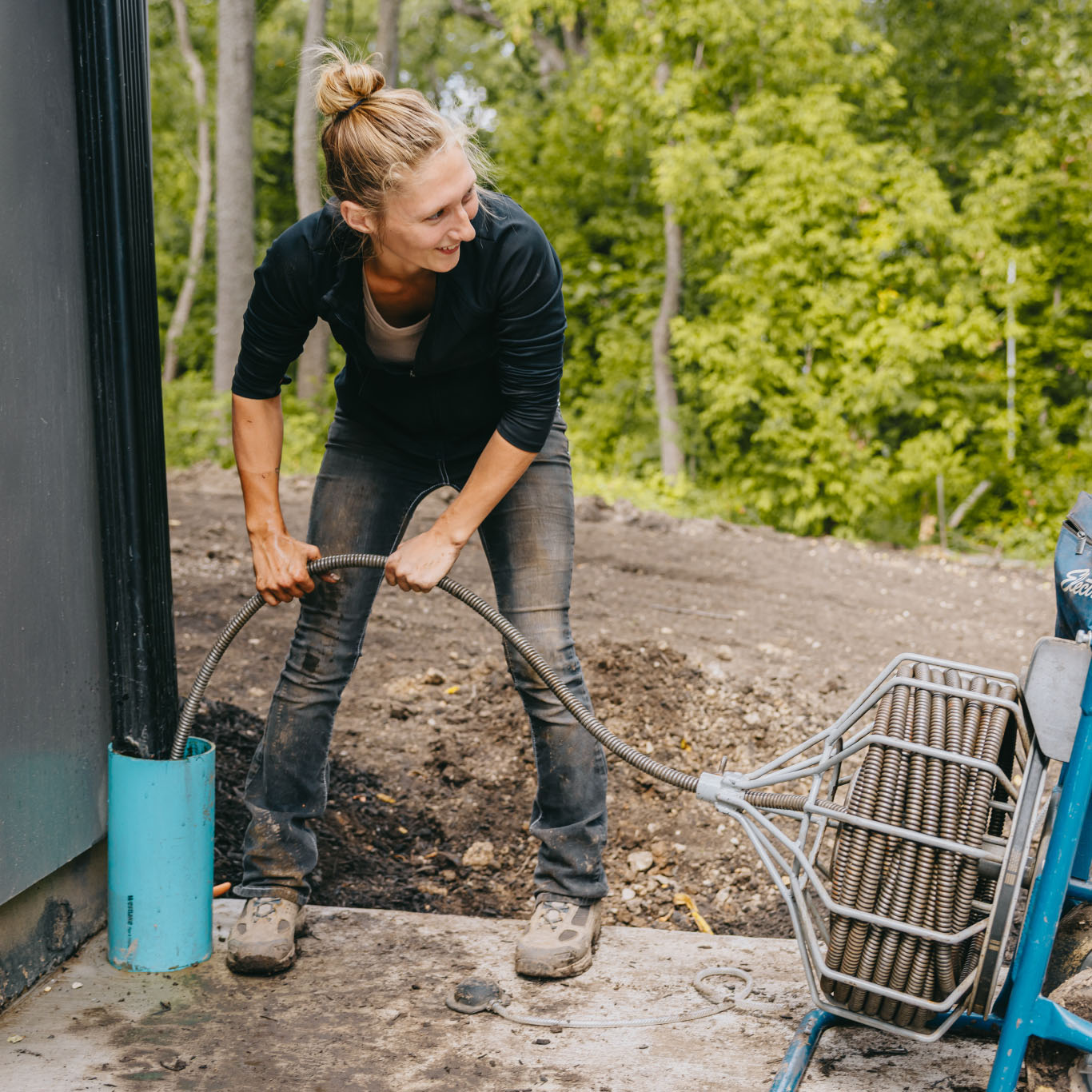 Female landscaper installing a flexible drainage pipe near a home foundation during landscape construction in the Chicago suburbs.