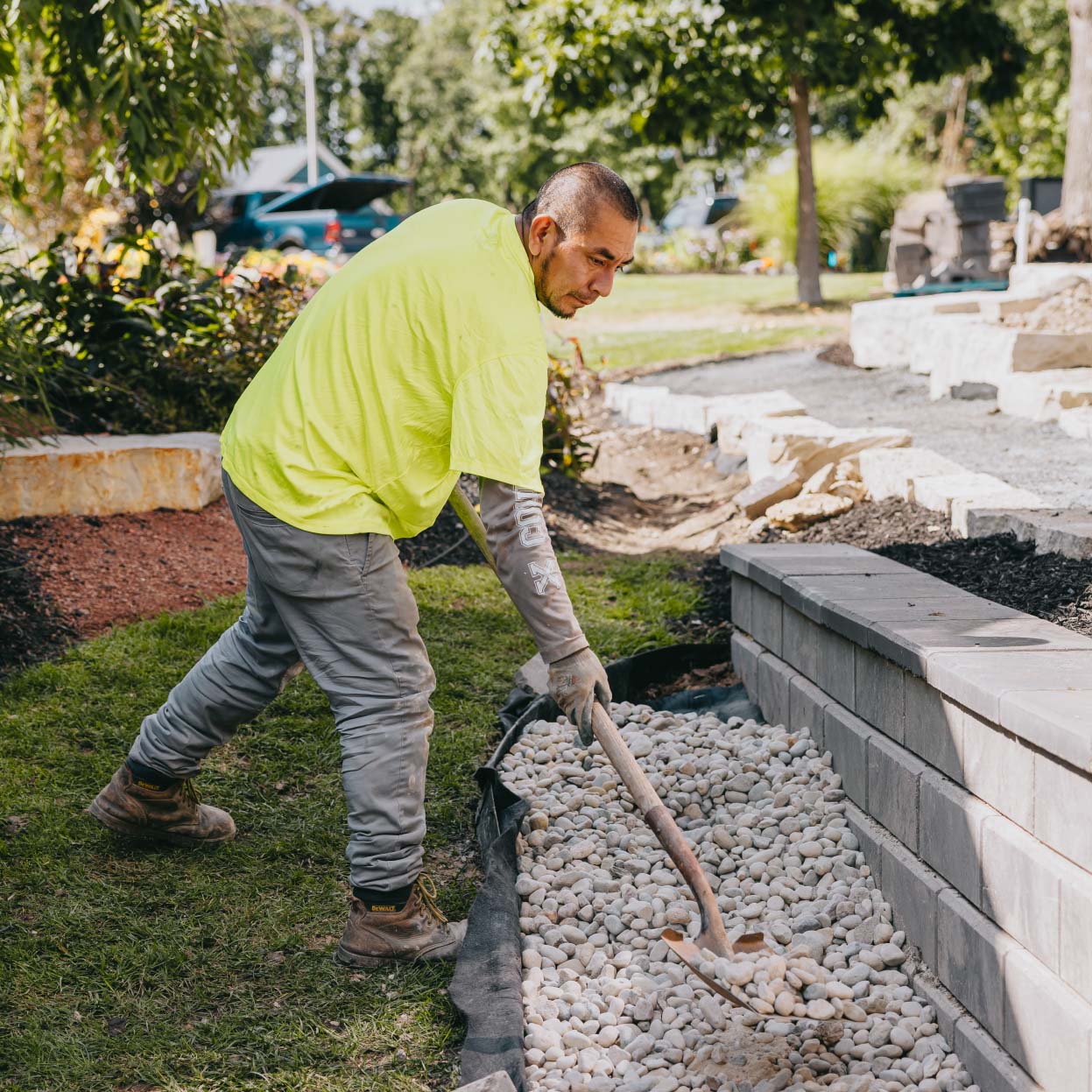 Landscape worker spreading white river stones along retaining wall for drainage and design in suburban Chicago.
