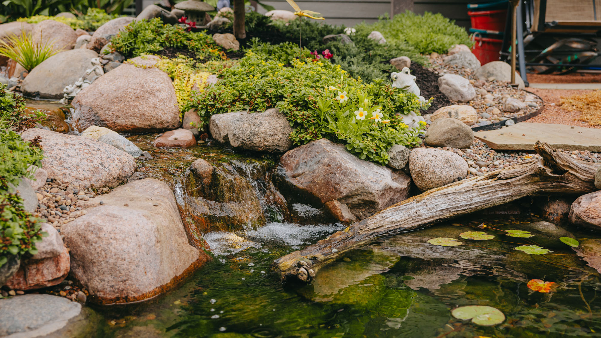 Backyard waterfall and stream surrounded by rocks, plants, and a pond in a custom landscape design in suburban Chicago.