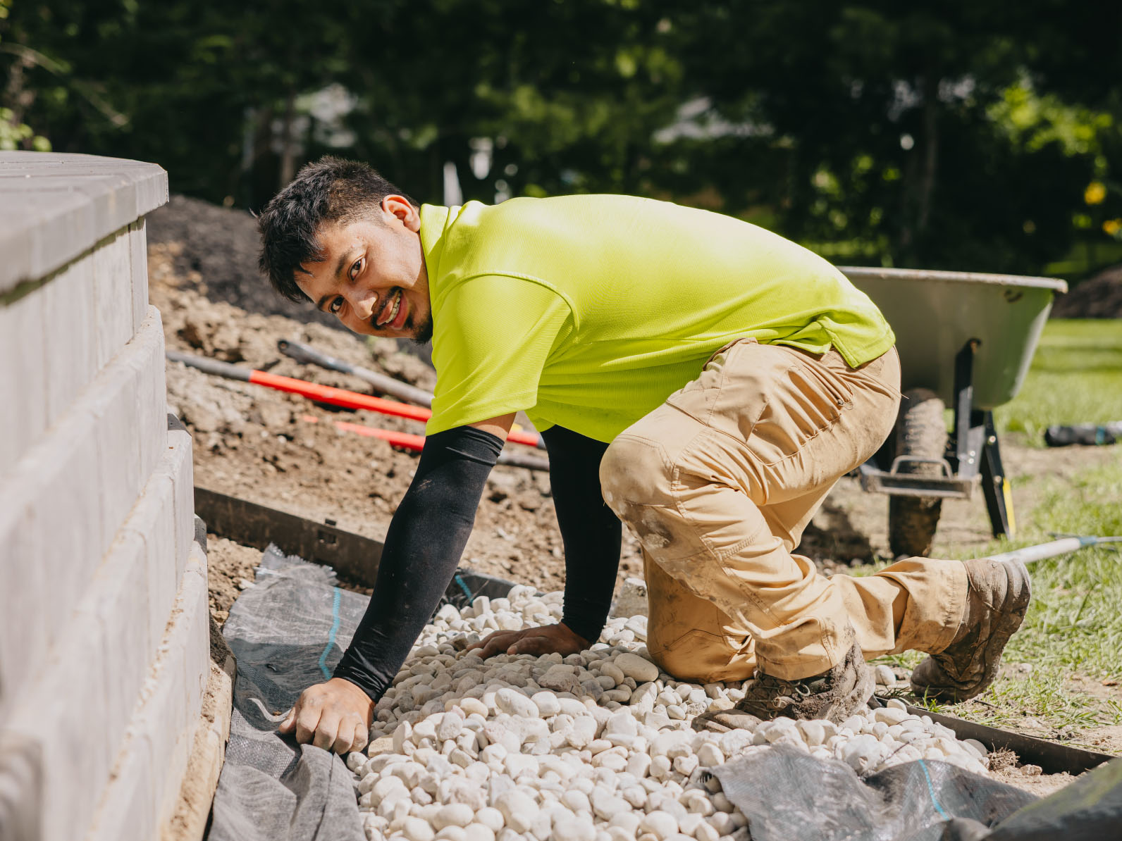 Smiling landscaper placing river rocks along retaining wall during landscape build