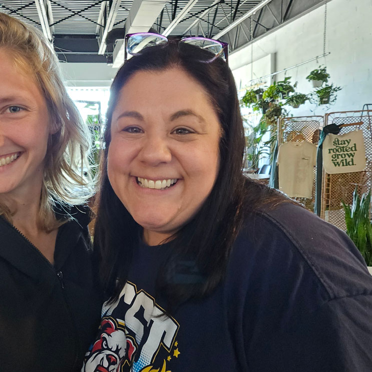 Two people smiling indoors near plants and decor, capturing a friendly client interaction at a design studio.