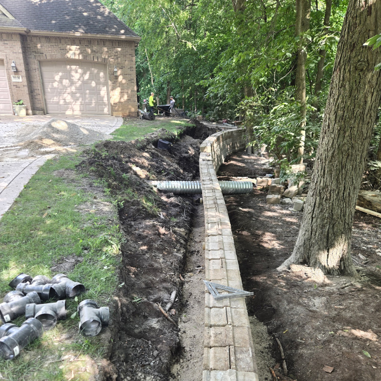 Construction of a long retaining wall with trenching and drainage pipe installation.