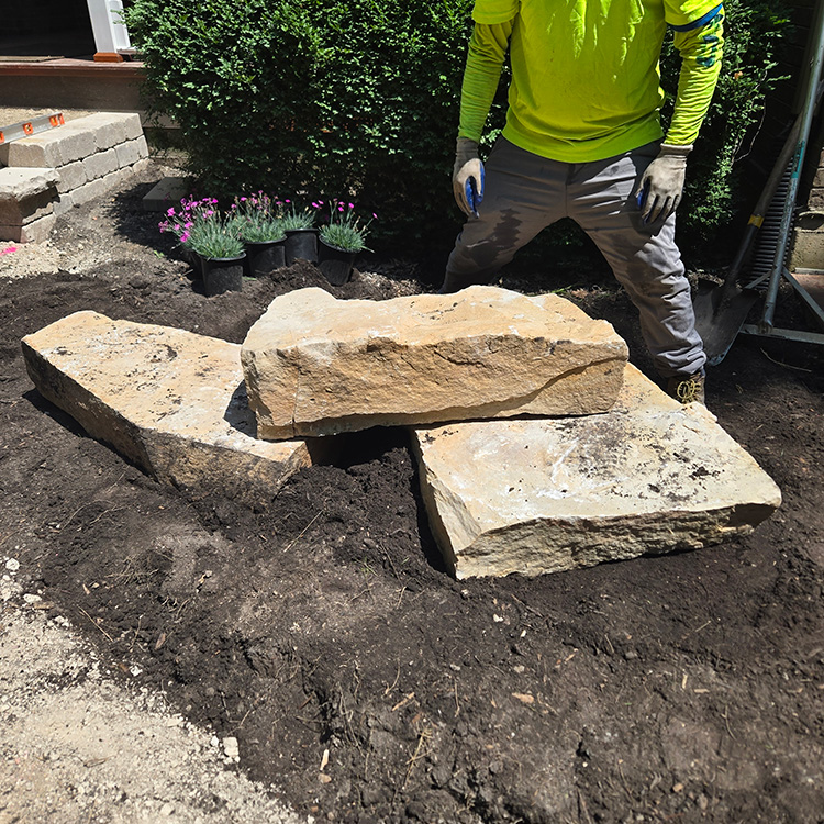 Crew member positioning large limestone boulders in a front yard landscape installation.
