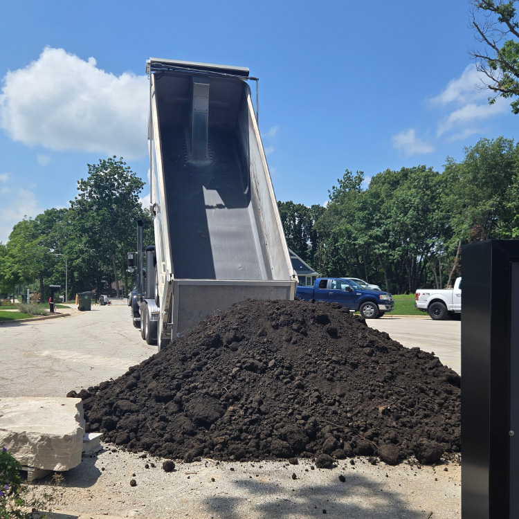 A dump truck unloading rich black topsoil for a residential landscaping project.
