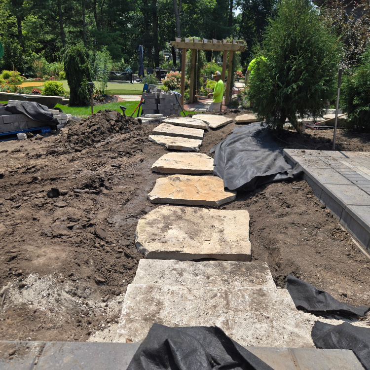 Workers laying large flagstone pieces to form a natural stone pathway in a landscaped backyard.