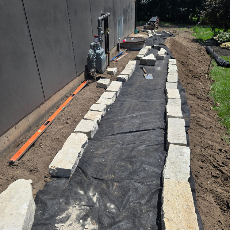 Early stage of a stone retaining wall installation with landscape fabric and leveling tools.