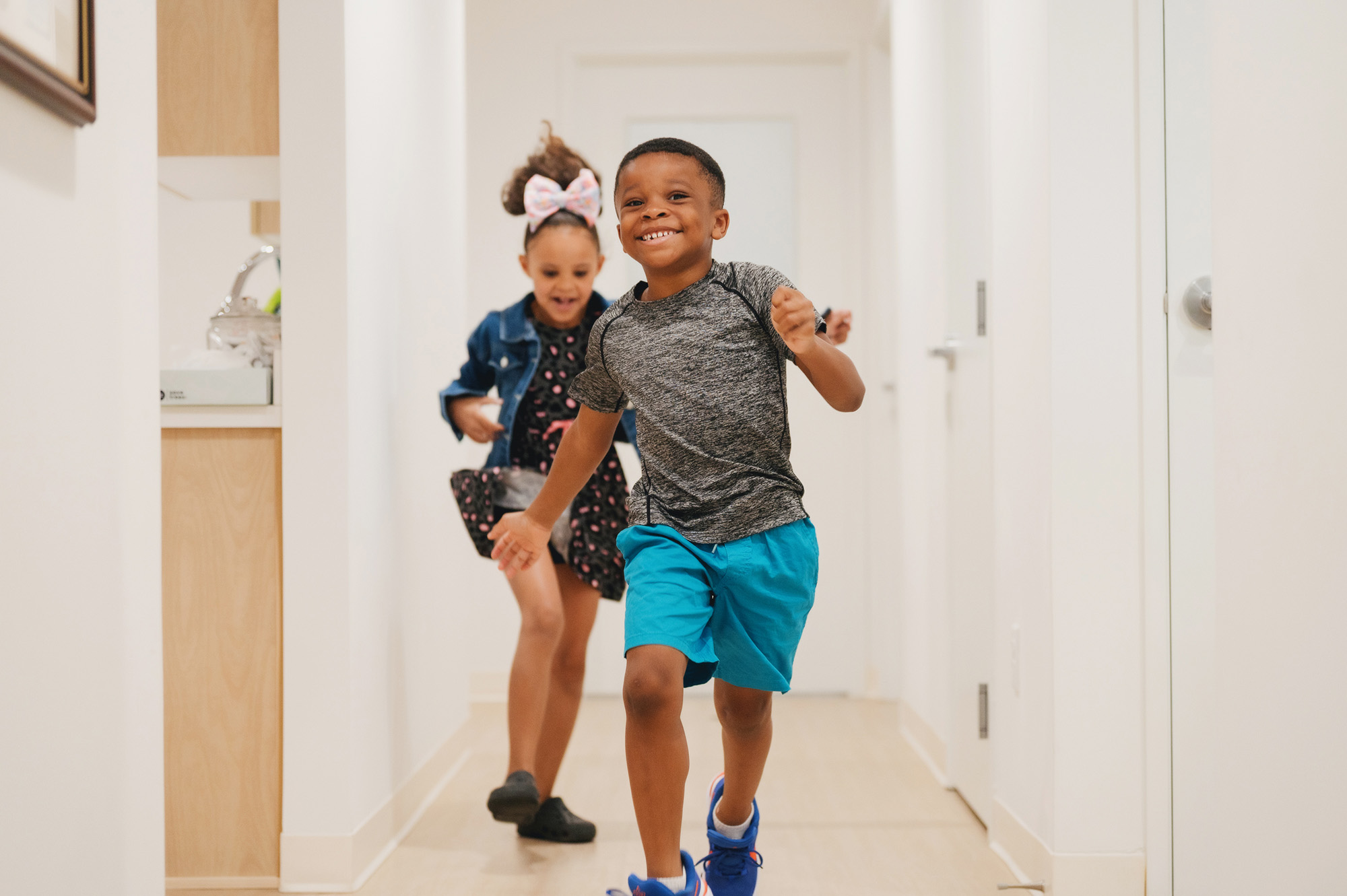 Two children running happily down a bright, narrow hallway inside a home.
