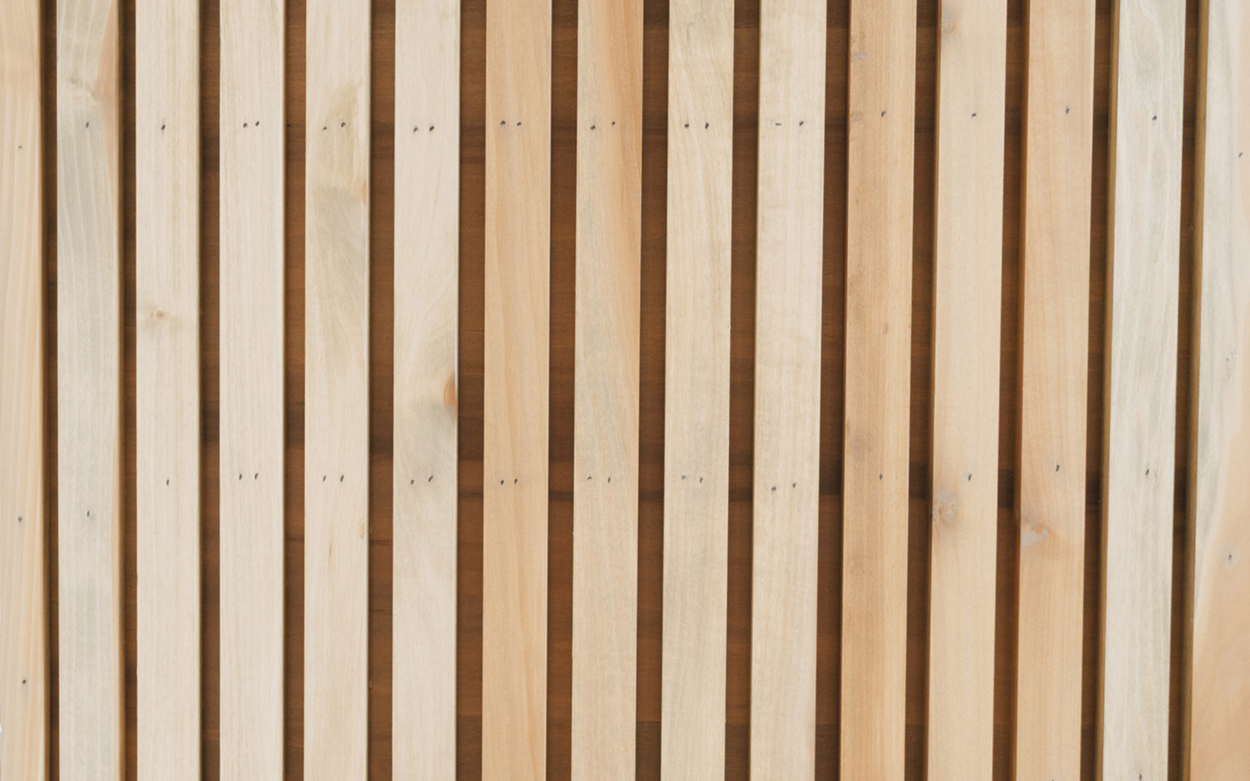Vertical wooden slats wall next to a white cabinet corner in a bright room.