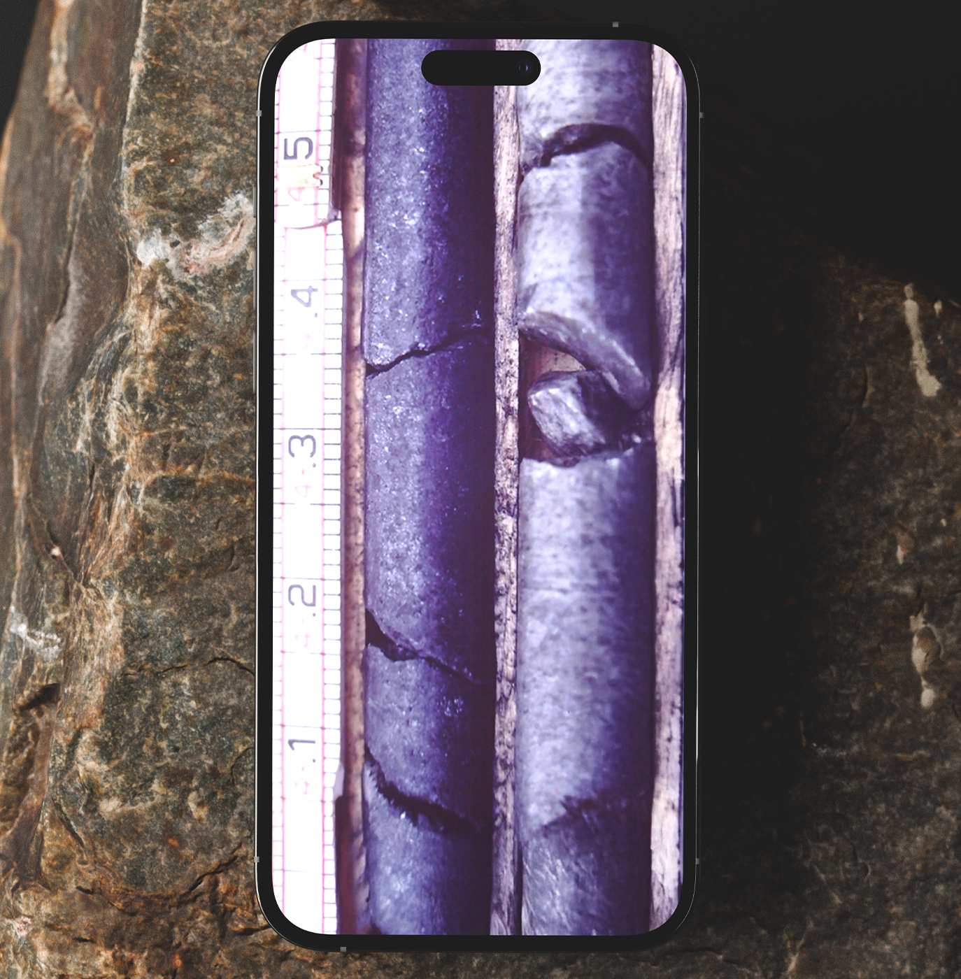 Two dark cylindrical rock core samples with visible cracks and fractures placed side by side next to a measurement scale.