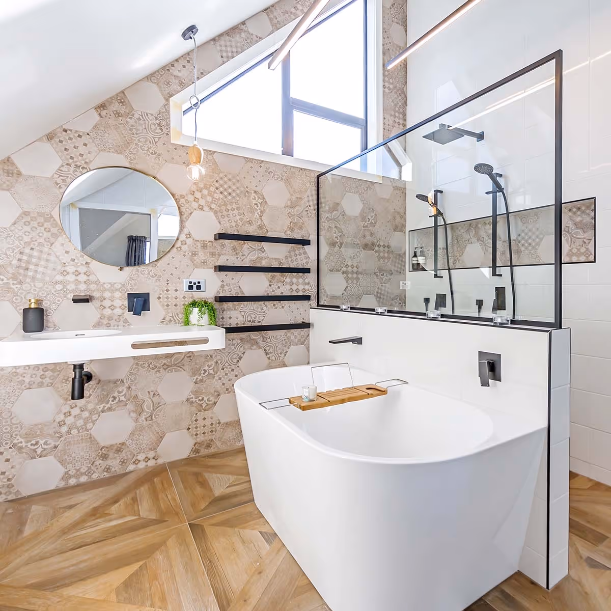 Modern bathroom featuring a freestanding tub, hexagonal patterned wall tiles, a round mirror, and sleek black fixtures. Natural light floods in.