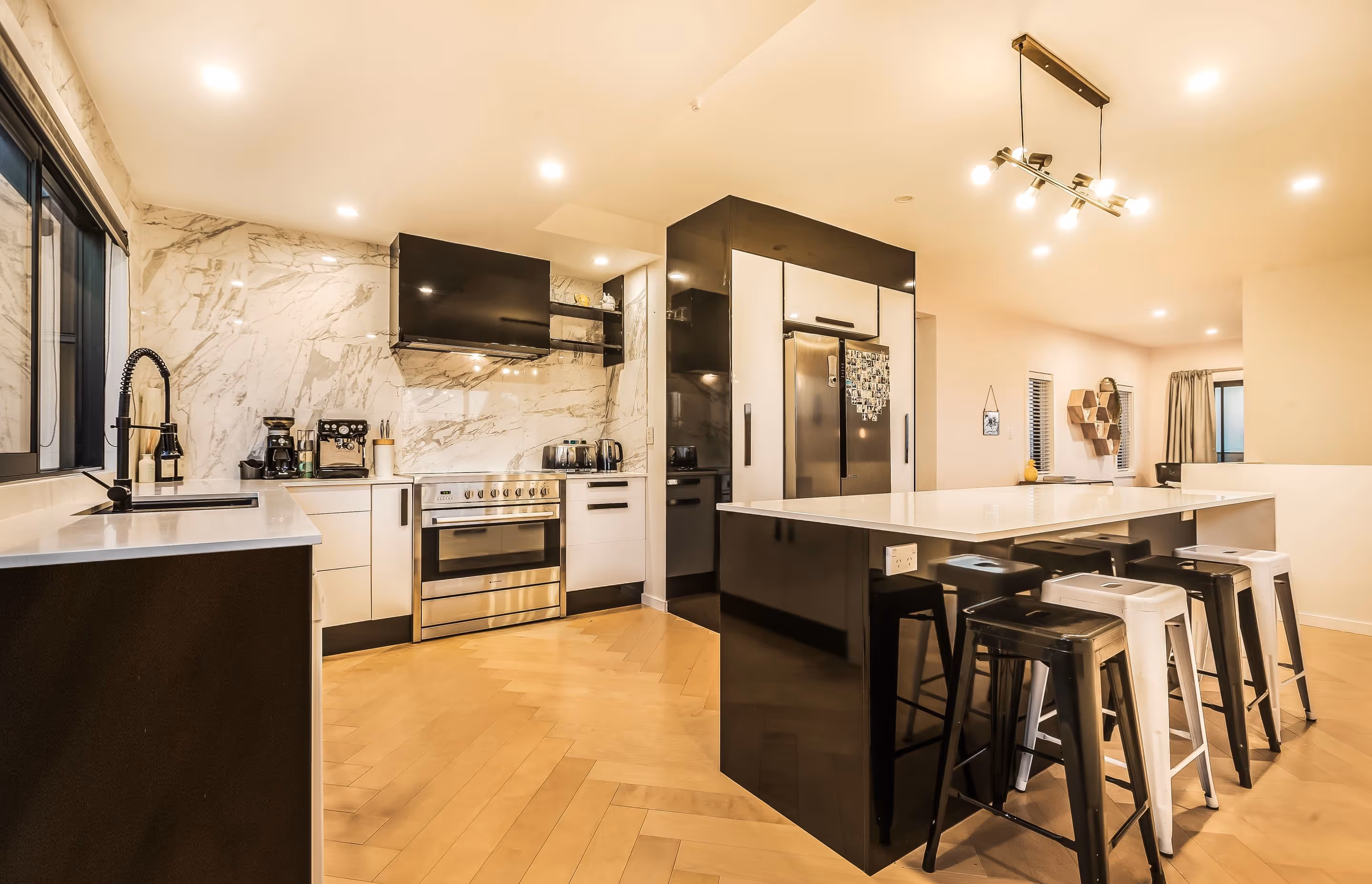 Modern kitchen featuring marble walls, sleek black and white cabinetry, stainless steel appliances, and stylish bar stools.
