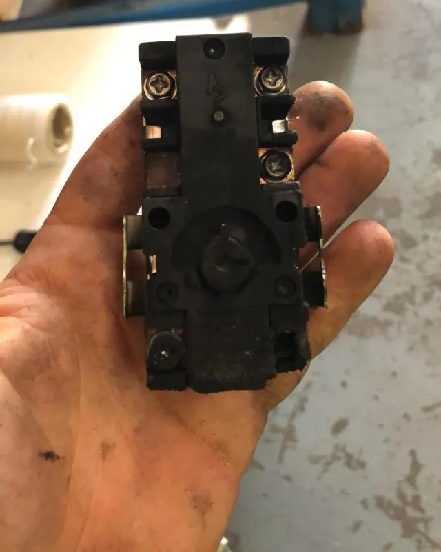 Hand holding a black electrical component with screws, against a grayish background.