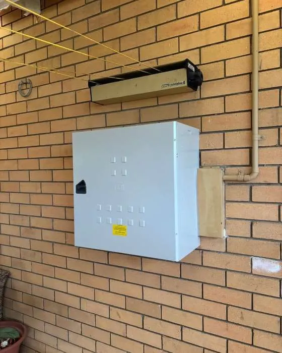 White electrical box mounted on a brick wall with a yellow sticker and a black handle.