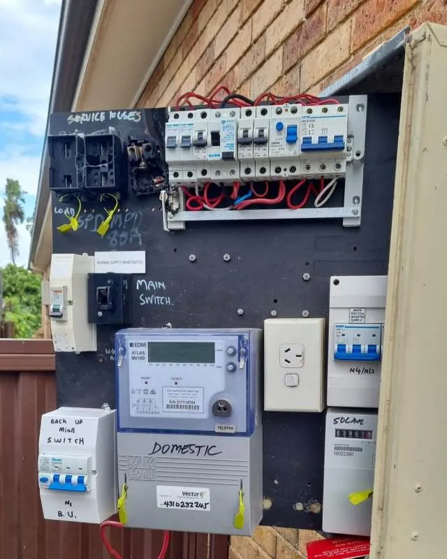 Electrical panel mounted on an outdoor wall with multiple circuit breakers, a domestic electricity meter, and labeled switches.