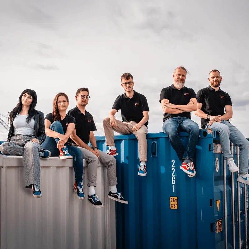 Das Team von m3 sitzt auf Seecontainer. Gruppenaufnahme