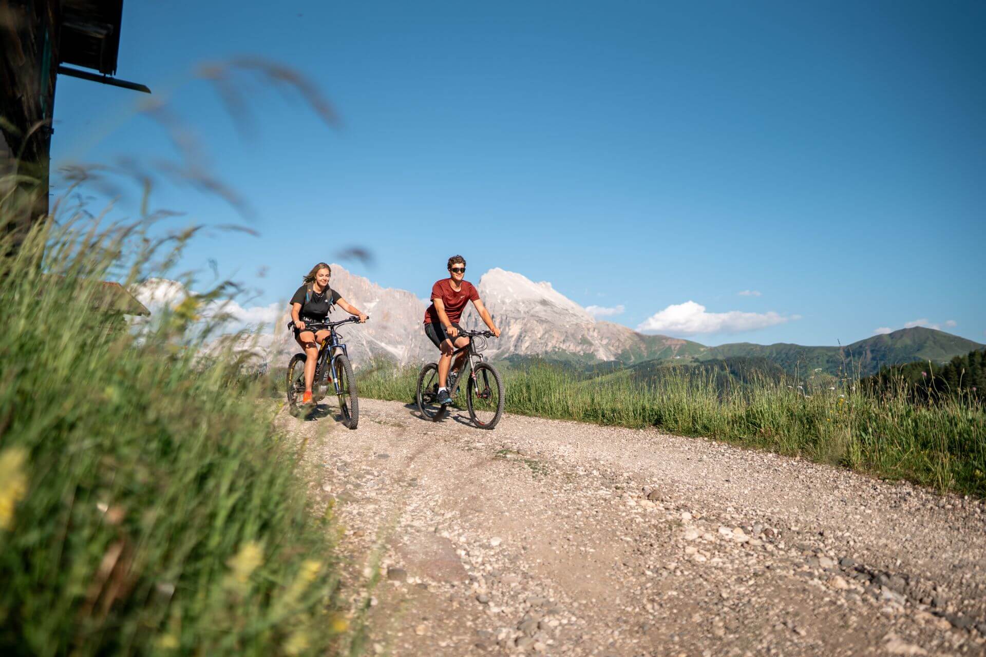Zwei junge Erwachsene auf einer E-Bike-Tour zur Laranzer Schwaige auf der Seiser Alm mit Blick auf die Dolomiten bei Sonnenschein.