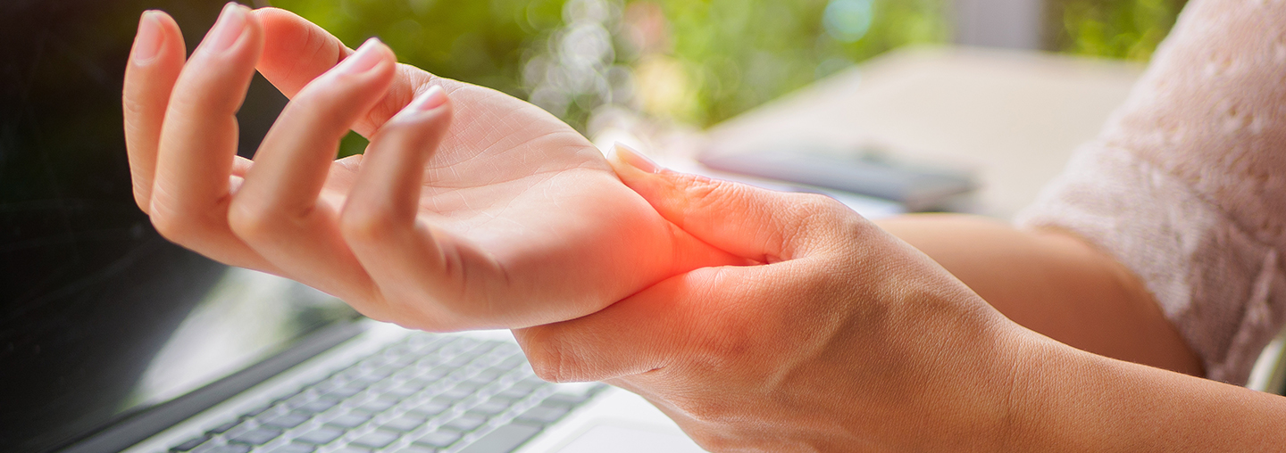 Person holding their wrist with one hand while sitting at a laptop keyboard.