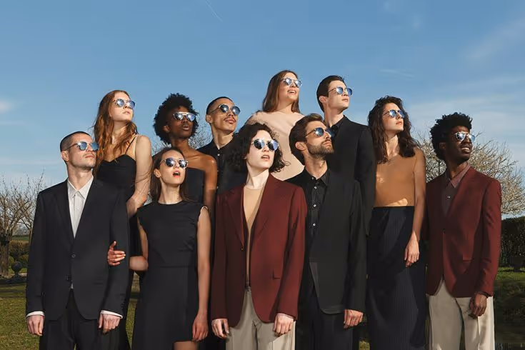 Group of ten young adults wearing sunglasses and stylish formal clothing standing outdoors under a clear sky.