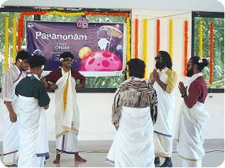 Group of people dressed in traditional white and maroon attire performing a dance inside a decorated hall.