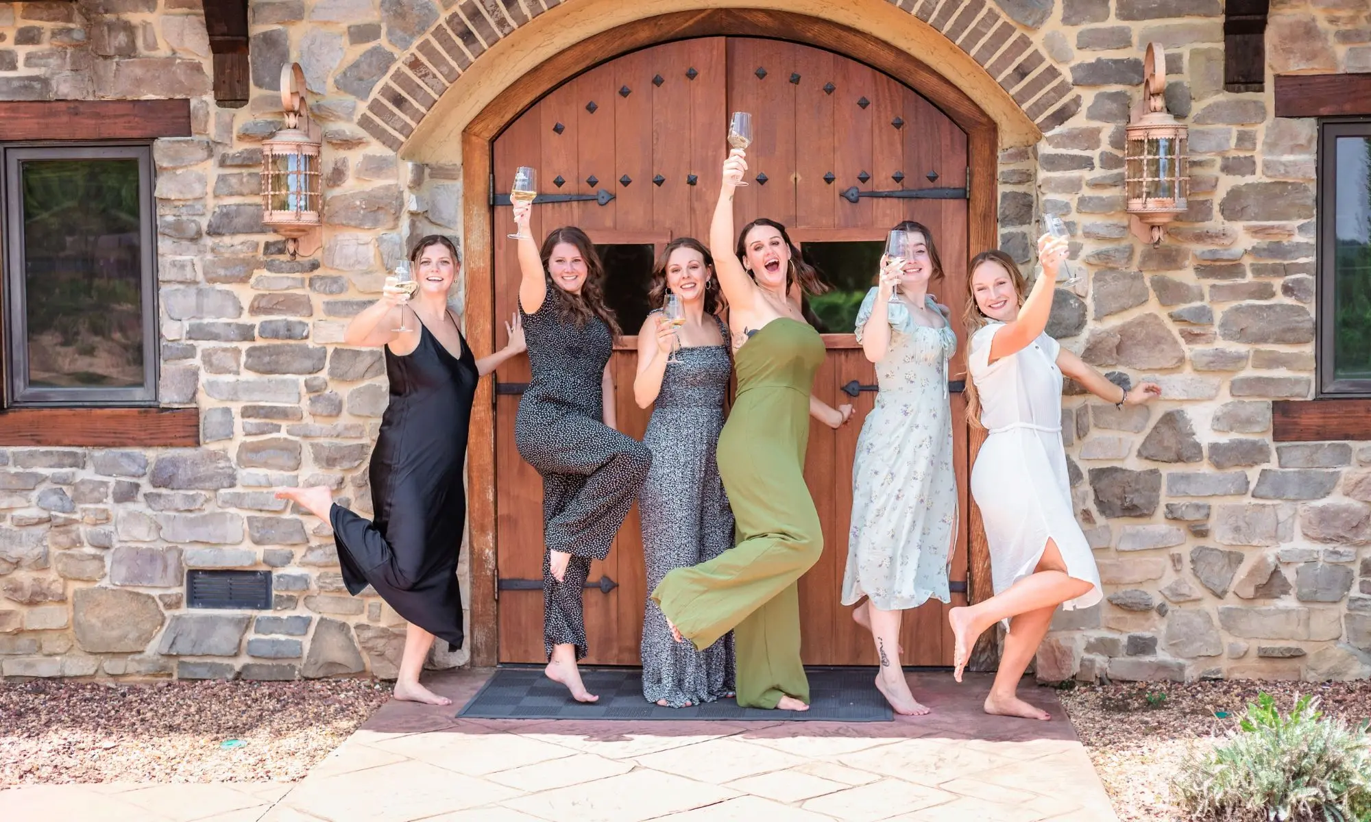 Group of women holding wine glasses posing in front of an arched stone entrance at Raffaldini Vineyards.