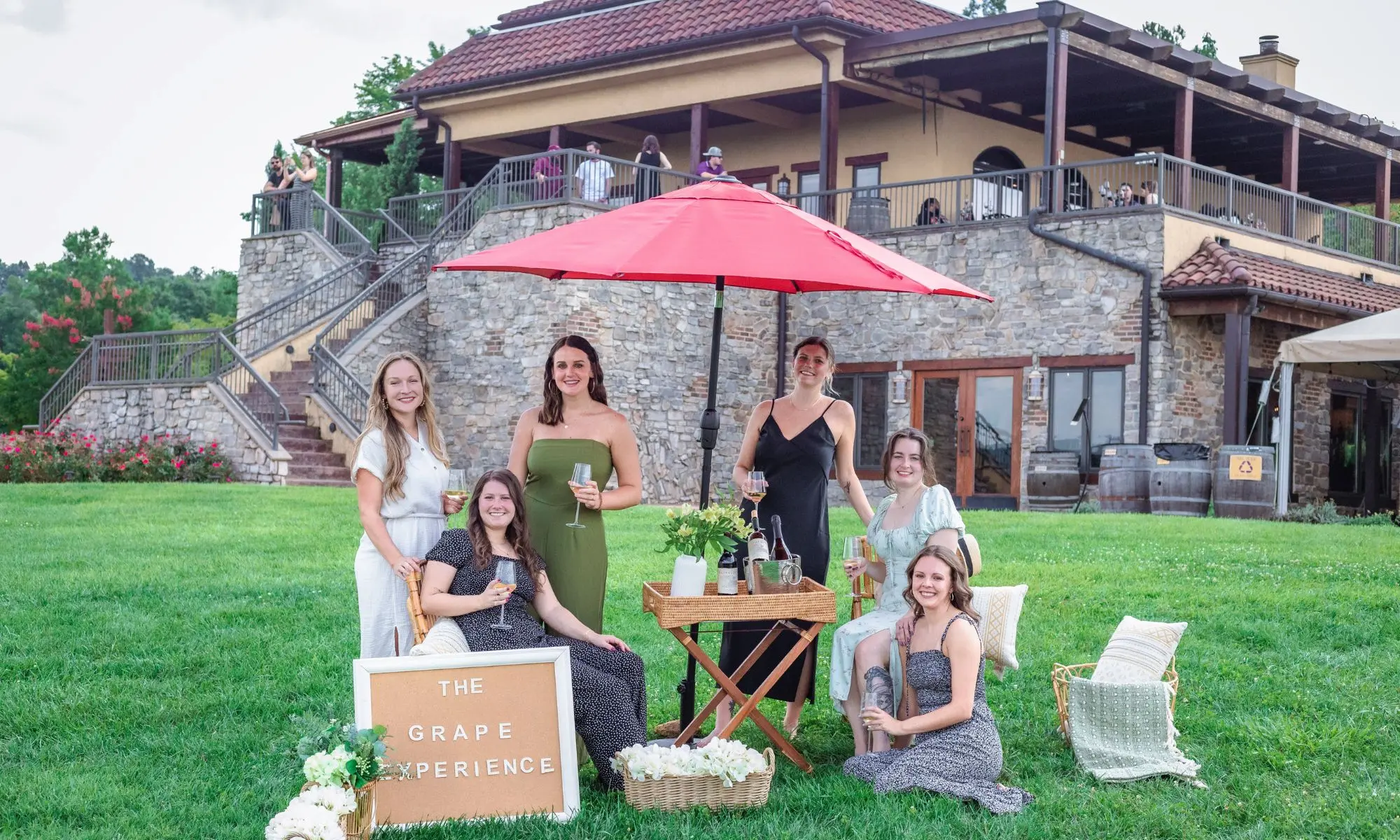 Guests enjoying a vineyard picnic with table setup, red umbrella, and Raffaldini Vineyards' estate building in the background.