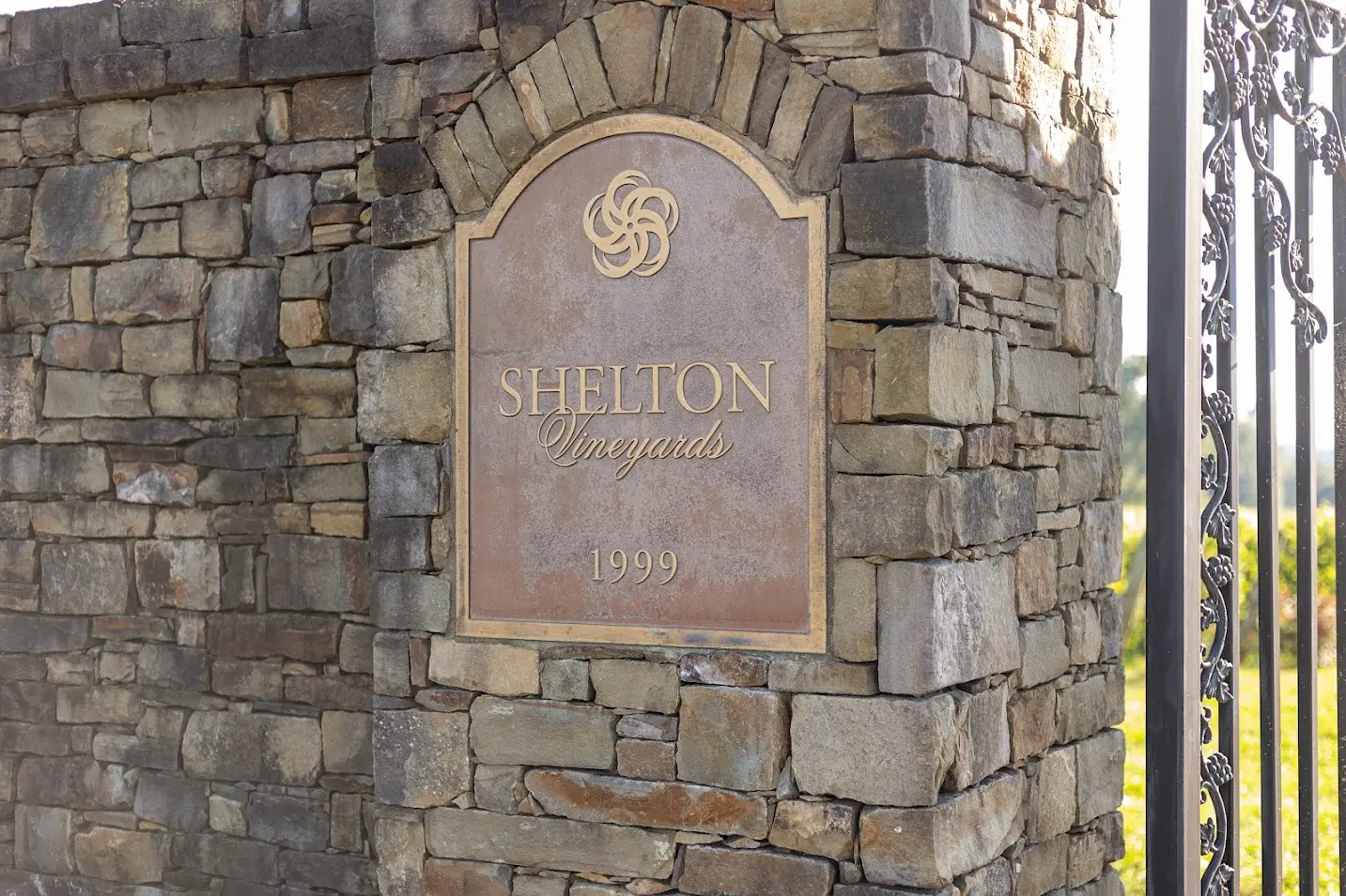 Stone entry marker with vineyard name plaque surrounded by green landscaping.