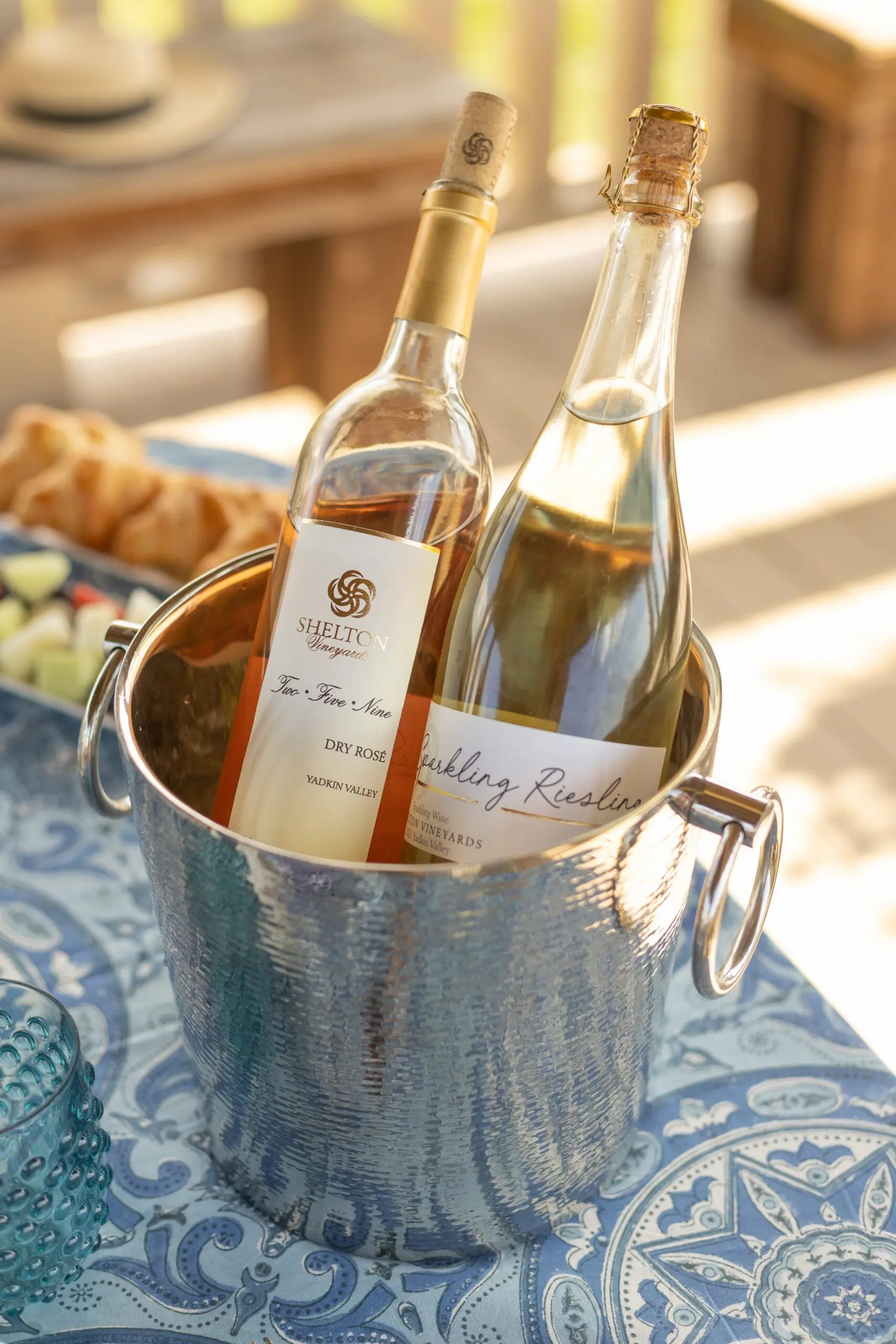 Wine bottle display with two bottles chilled in ice bucket on small wooden table during vineyard picnic.