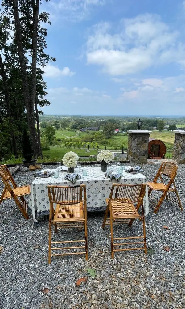 Outdoor vineyard picnic setup with wooden chairs, table, and scenic vineyard backdrop.