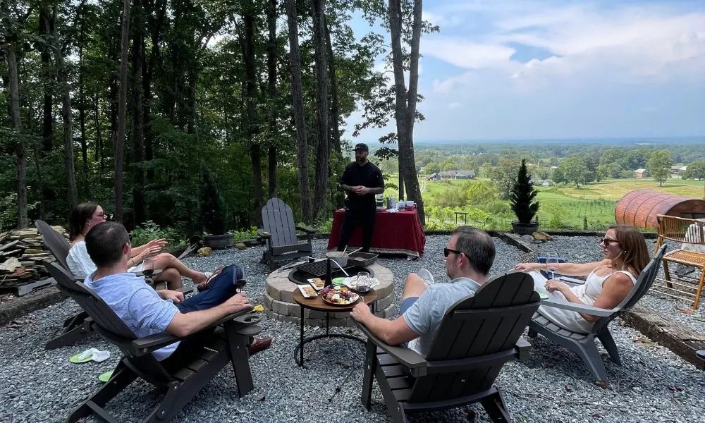 Group of people relaxing on outdoor lounge chairs with vineyards and trees in the background.
