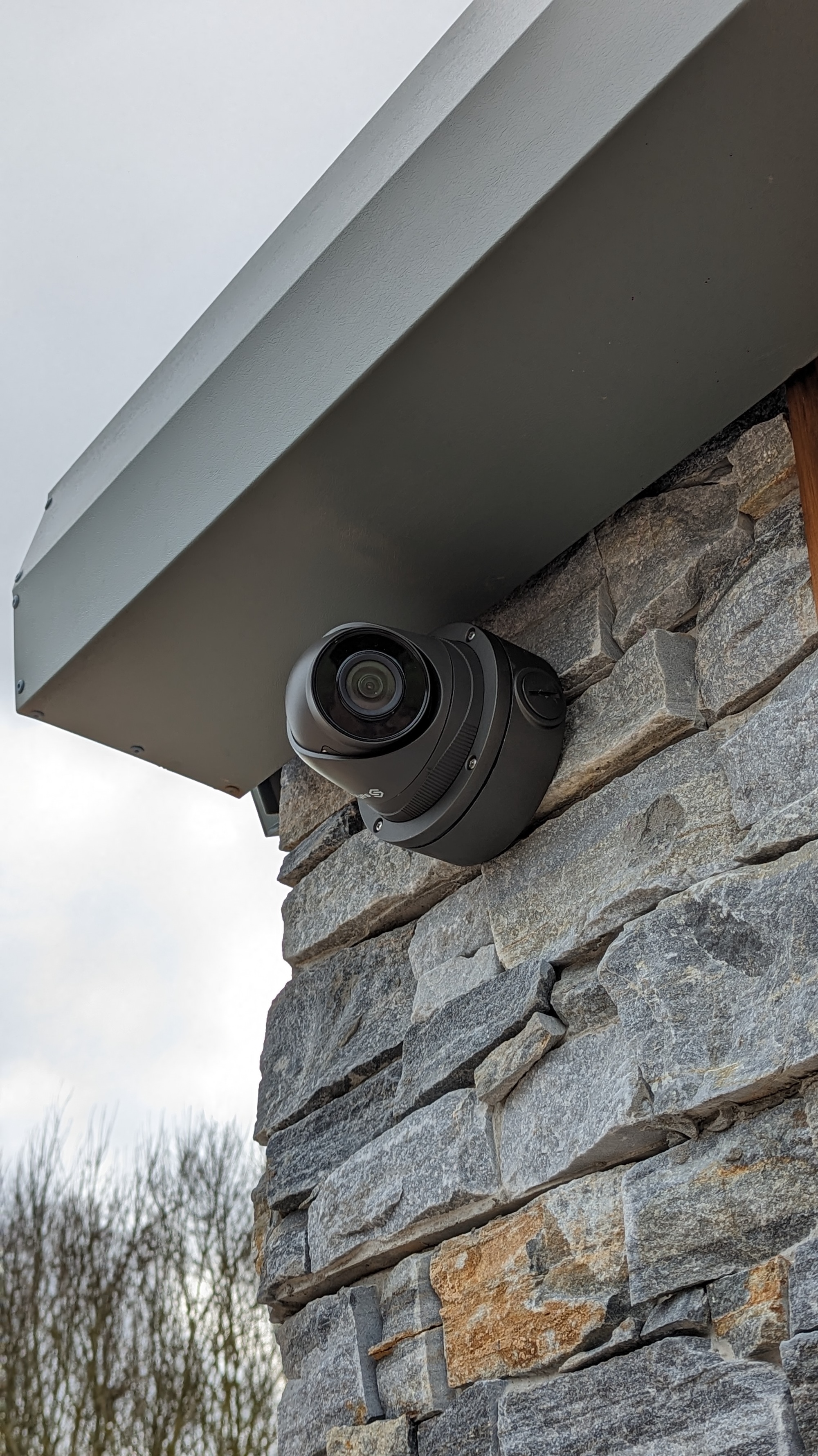 A discreet dome security camera mounted beneath the eaves on a stone facade — quiet, watchful protection.