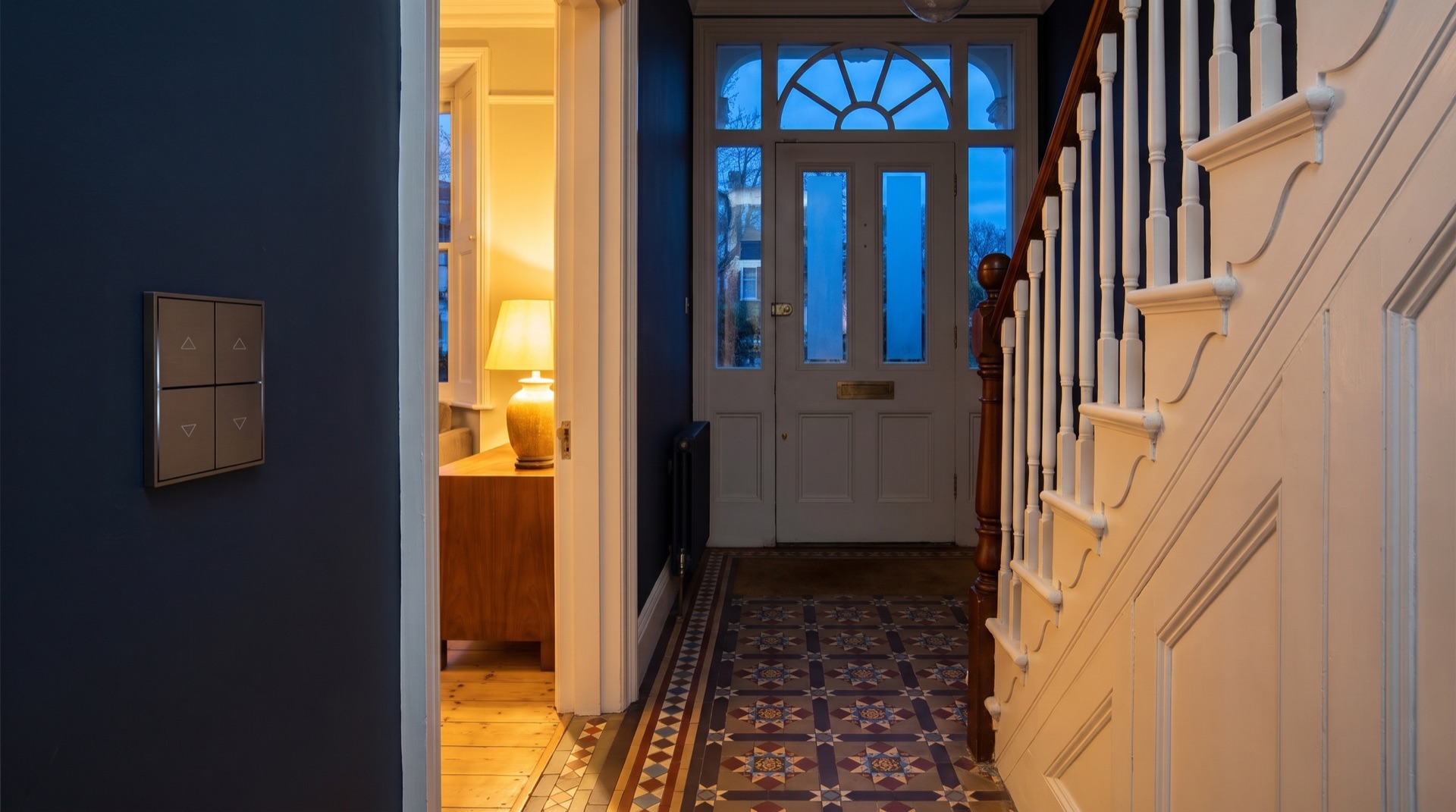 Bronze lighting scene switch on a navy wall in a Victorian townhouse hallway at dusk, KNX vs Control4