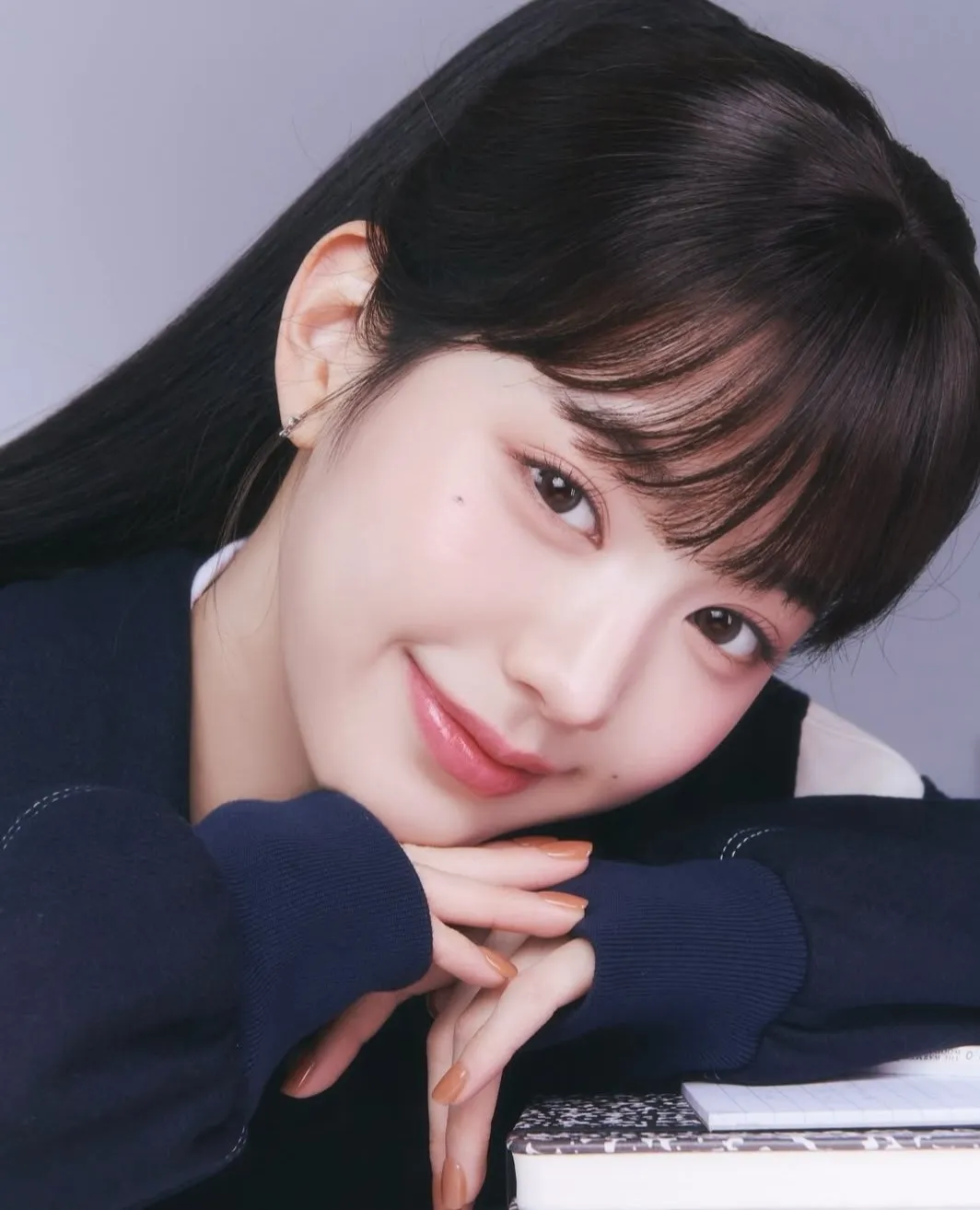 Woman with dark hair and bangs resting her chin on her hands, smiling softly, wearing a navy sweater.