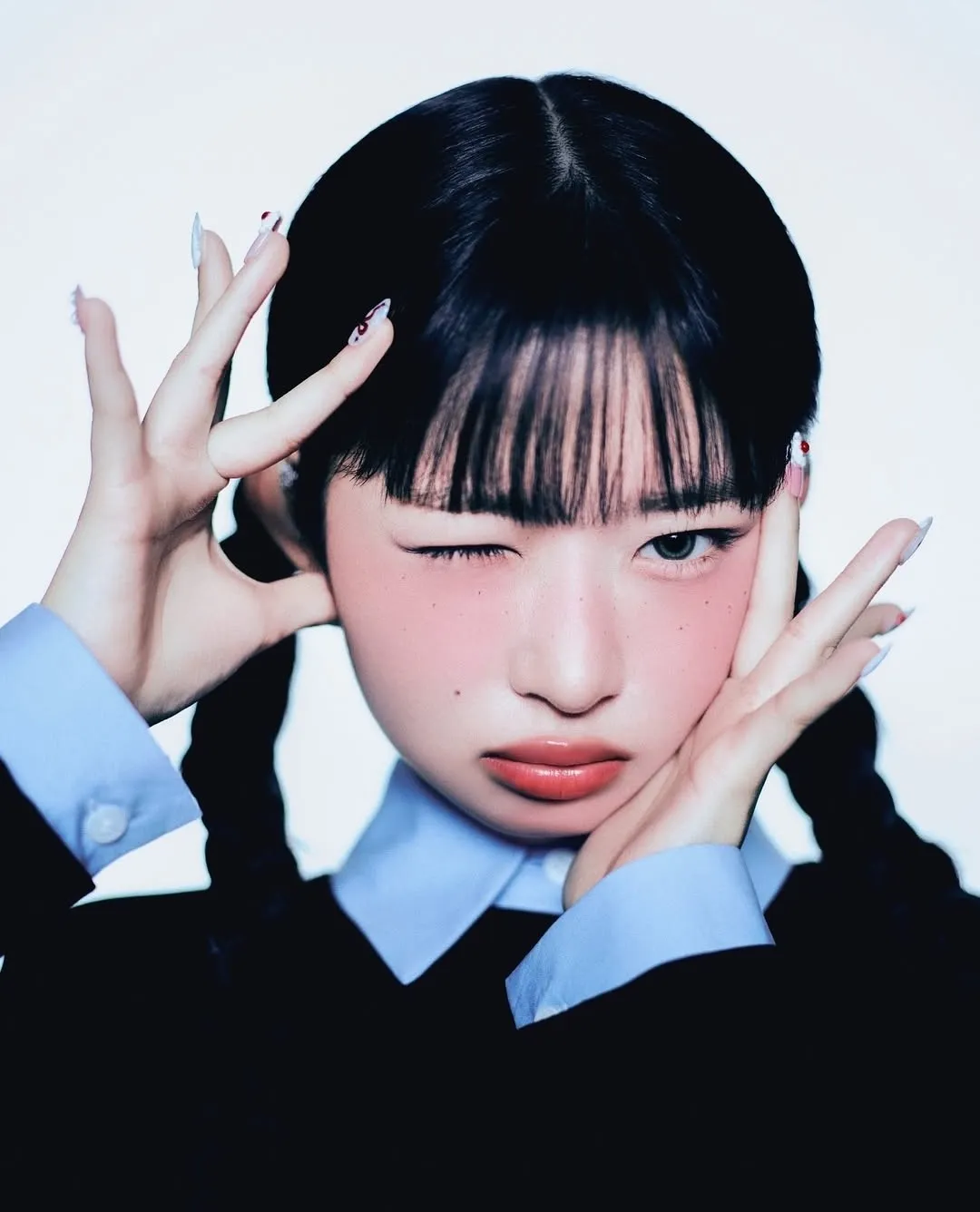 Close-up of K-pop idol with braided hair and blunt bangs winking and posing with expressive hands.