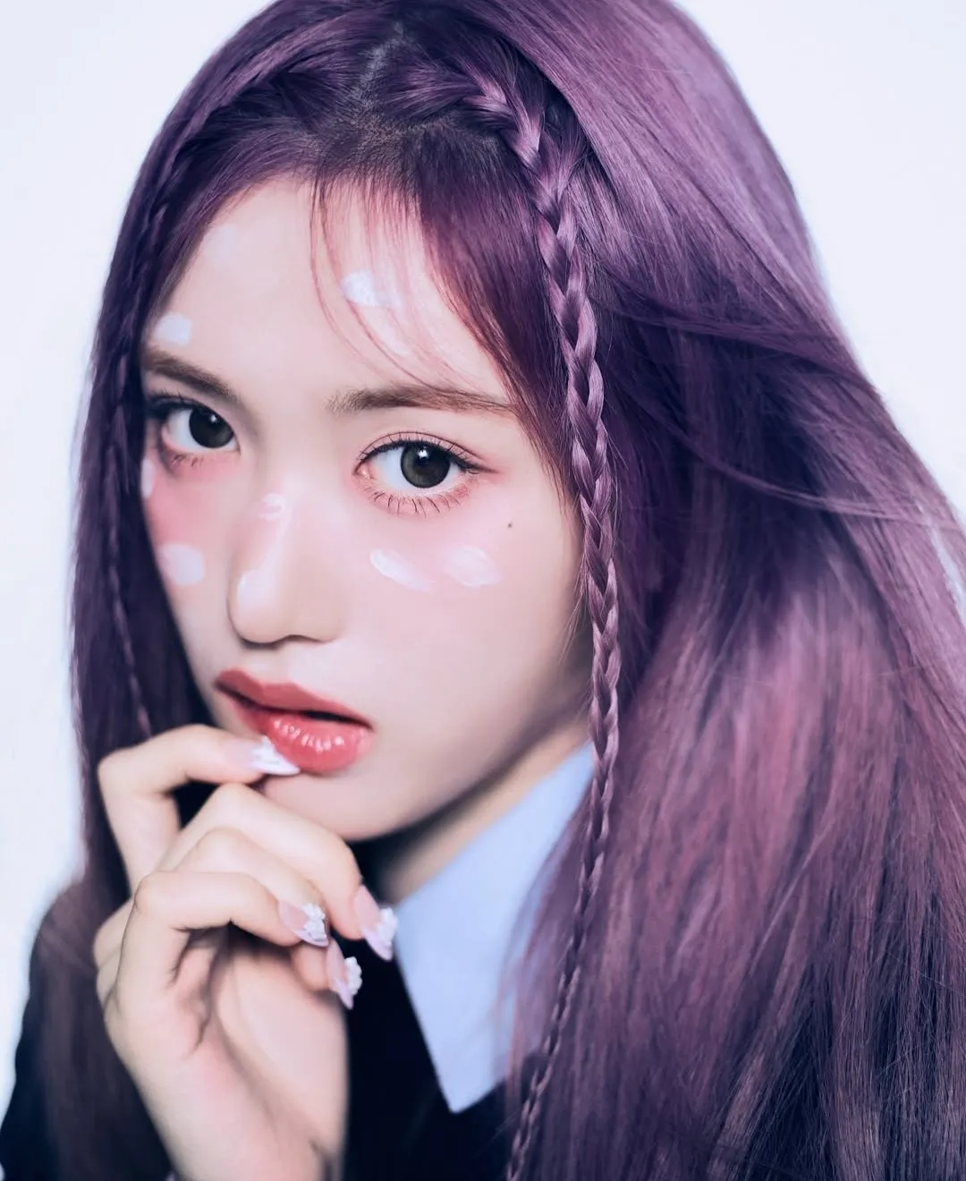 K-pop idol with long purple hair and face paint details gazing intensely at the camera.