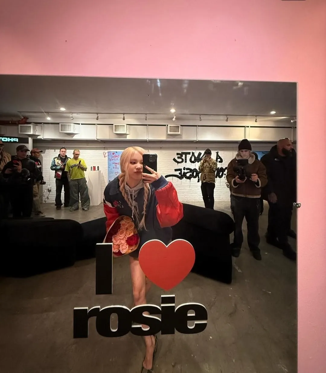 Blonde taking selfie in front of "I Heart Rosie" sign with bouquet