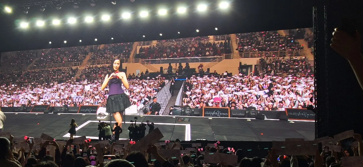 isoo making a heart gesture on stage with a large cheering crowd holding banners at a Vietnam concert.