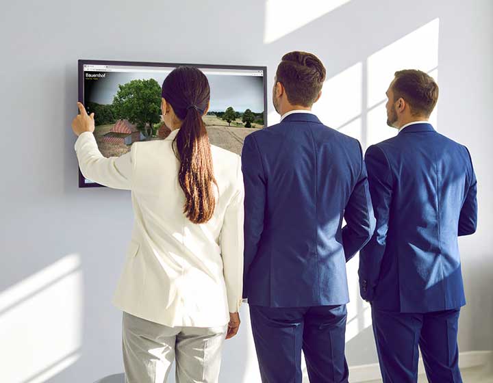 Immobilienmakler vor einem Monitor an der Wand