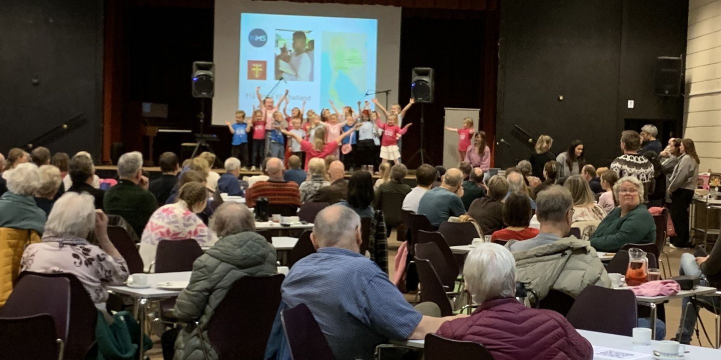 Bildet viser publikum som ser et barnekor som framfører sanger fra en scene