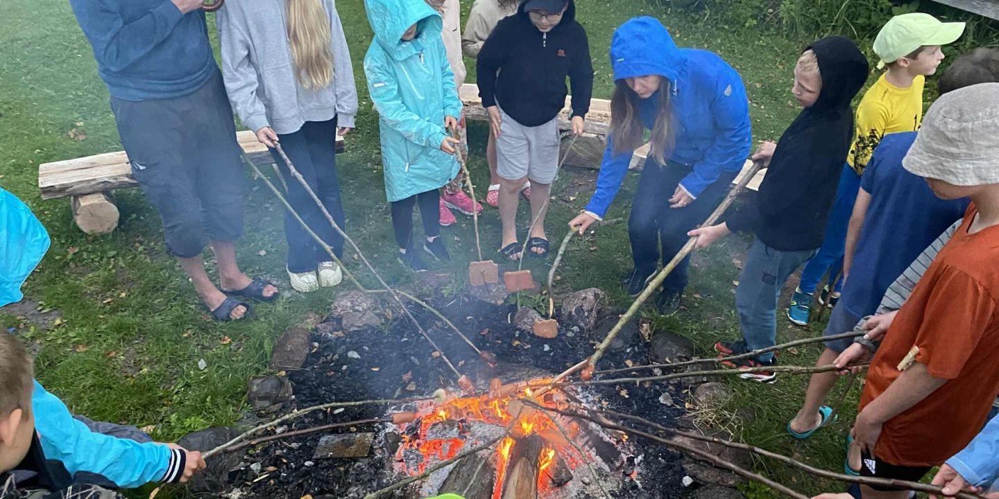 Bildet viser barn som står i ring rundt et bål og griller