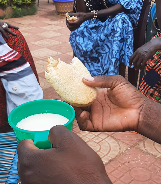 Bildet viser ei hånd som holder et stykke brød over en grønn kopp med drikke
