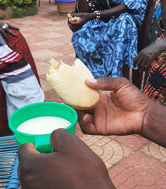 Bildet viser ei hånd som holder et stykke brød over en grønn kopp med drikke