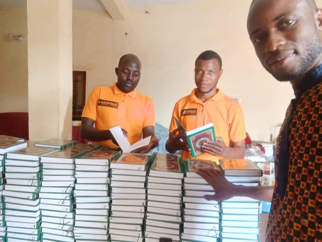 Bildet viser tre personer fotografert sammen med en bokstabel av mosebøkene oversatt til fulani