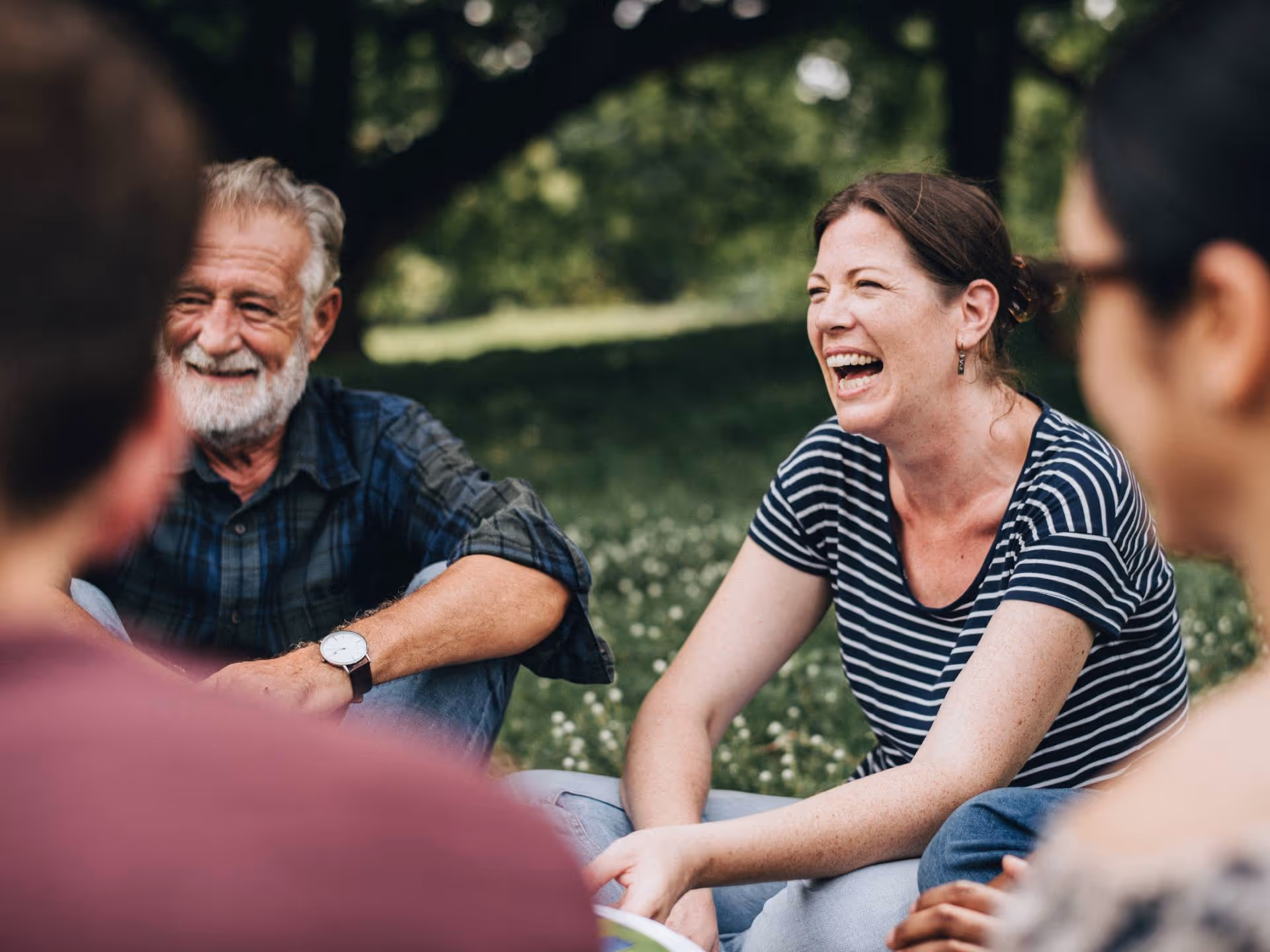 Bildet viser smilende personer som sitter i ring utendørs