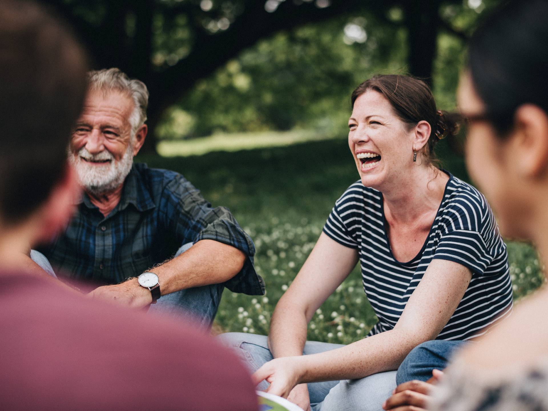 Bildet viser smilende personer som sitter i ring utendørs
