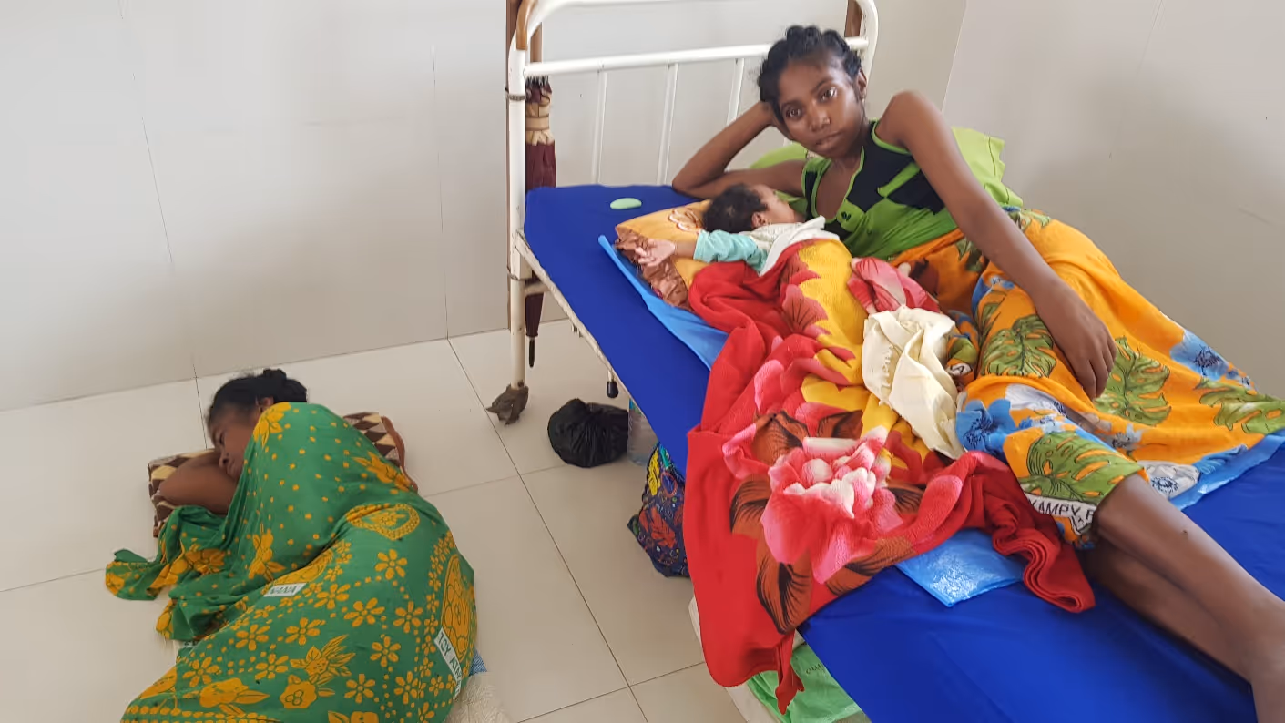 Bildet viser en kvinne med babyen i senga, foran på gulvet ligger mora