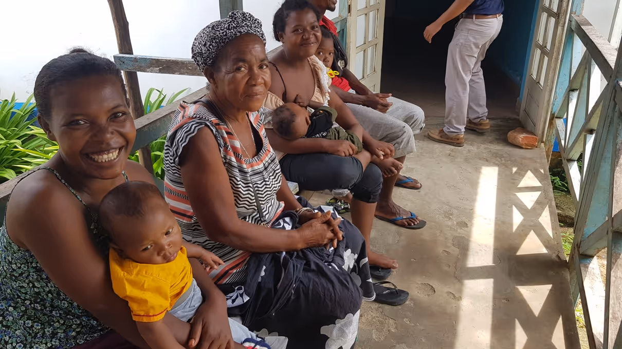 Bildet viser flere kvinner med barn som sitter på en benk og venter